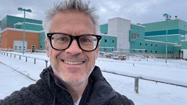 A man stands in front of a hospital. 