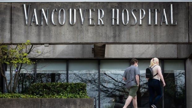 Two people wearing facemasks walk towards a building marked 'Vancouver Hospital' in large letters.