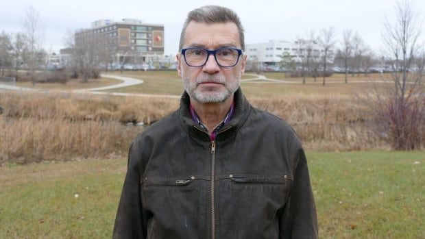 A man in a black jacket and glasses looks forward.