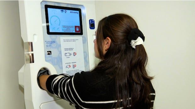 CBC's Brittany Henriques puts her arm into a tall machine on a wall with a screen on it