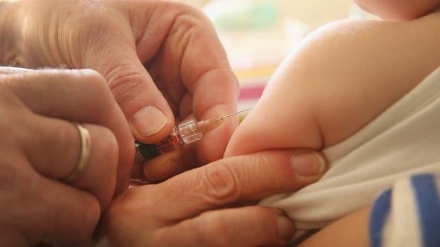 A closeup of a man administering a vaccine to an infant.