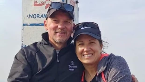 Man and woman wearing black caps pose for picture. 