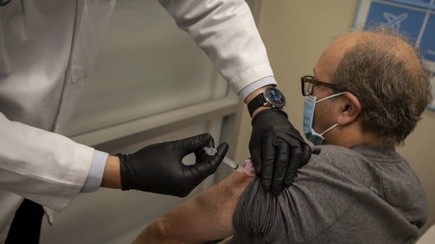 Man in chair facing away from camera gets flu shot in his arm