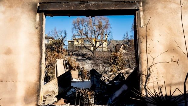 A home destroyed by fire stands in front of a home that survived.