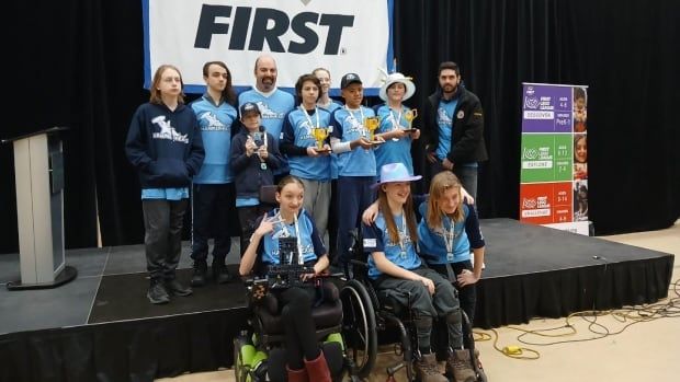 A group of 10 kids and two adults, some in wheelchairs and others on a small stage holding trophies made of Lego.