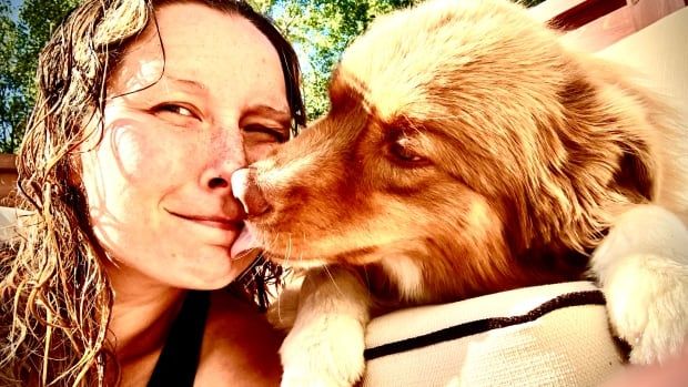 A woman smiles as an Australian Shepherd dog licks her face playfully