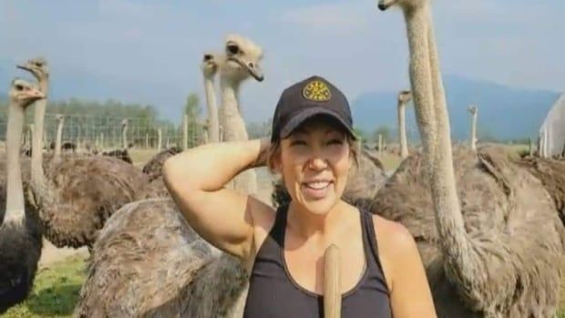 A woman smiles in a field with ostriches.