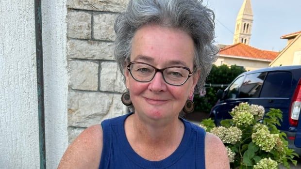 Woman smiles into the camera wearing a blue top and is outside.