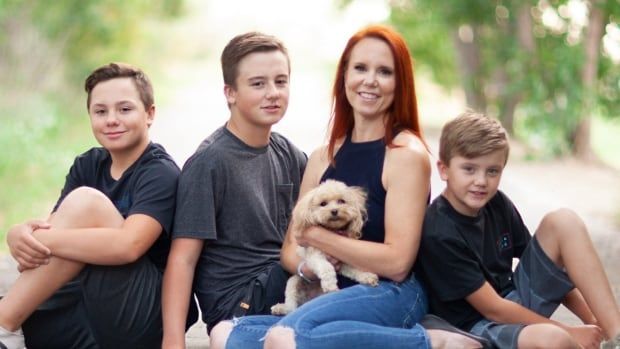 A red-headed woman holding a dog sits on the floor, surrounded by three young blonde boys.