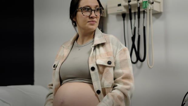 A pregnant woman poses for a photo in a doctor's office. 