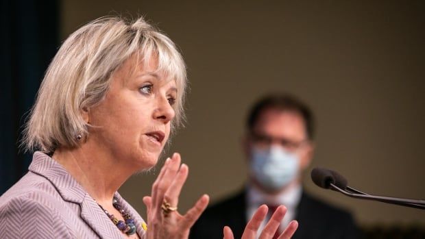 A white woman gestures at a podium while a masked man stands in the background.