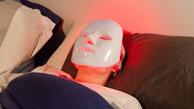 A person wearing a white mask with glowing red lights lies on a bed