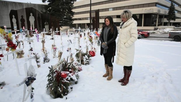 Two women look at rows of crosses.