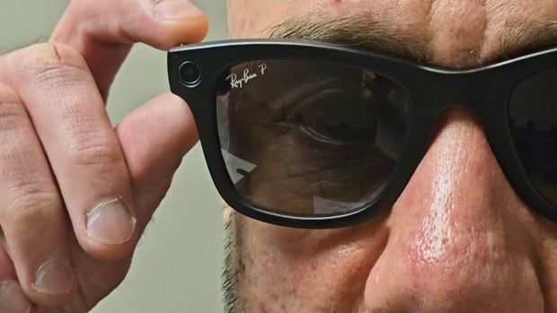 A close shot of a man's face with a pair of Meta Smart Glasses, showing the Ray Ban logo in the corner. 