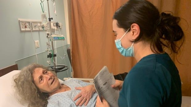 An elderly woman in a hospital bed talks to a younger woman who is standing up.