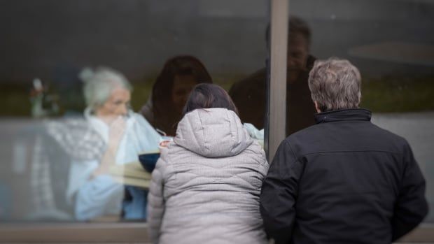 A woman and a man look through the window of a long-term care home because they can't go inside to be with their loved one. 