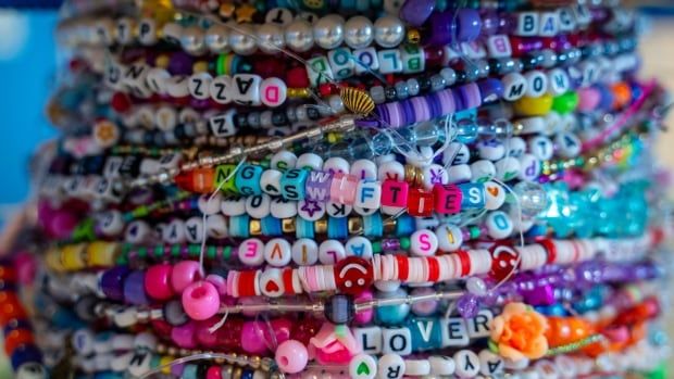 A close up image of a wrist crowded with bracelets is shown. The beads spell out words including 'LOVER,' 'SWIFTIE' and 'BAD BLOOD.'