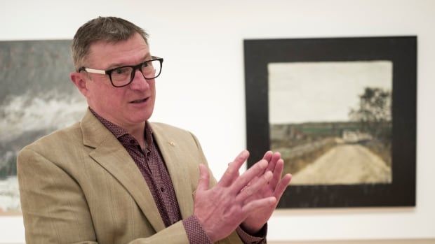 A man gestures in front of a painting.