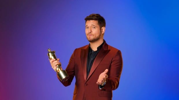 Michael Bublé wears a maroon suit while looking confused and holding a golden Juno Award.