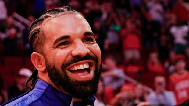 Drake smiles while wearing a blue jacket at a sports game.