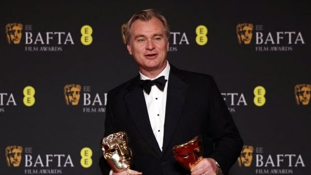 A person in a tuxedo holds two awards. 