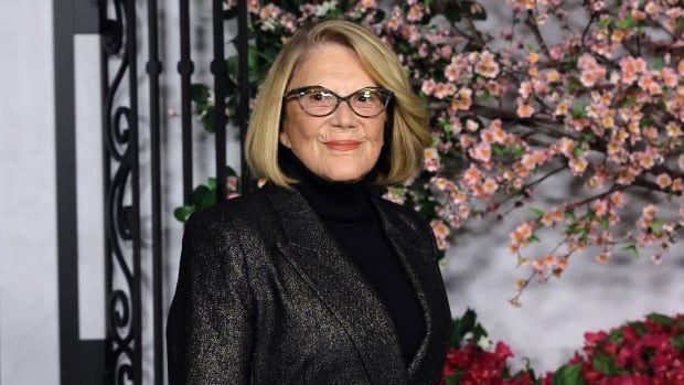 A woman is pictured smiling wearing glasses and a suit jacket. 