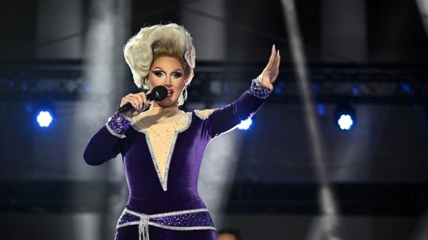 A performer in drag makeup sings on stage. 