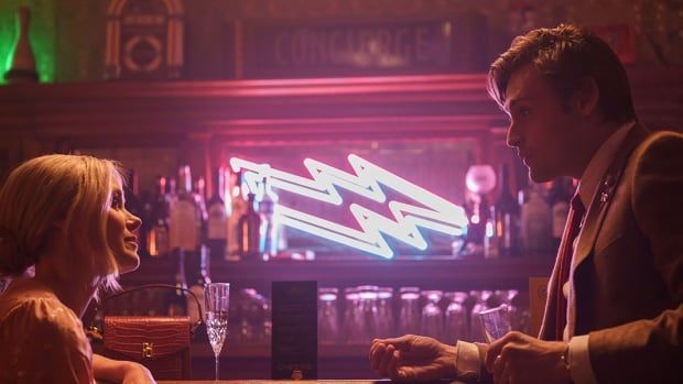 A young man and woman face each other, talking inside a neon-lit bar. 