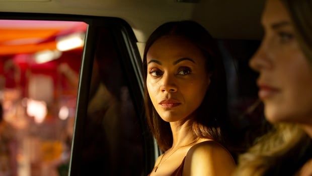 Two women in a car. One looks forward while the other is turned toward her. 