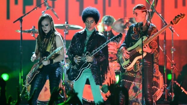 A man and two women stand side by side playing guitars on a concert stage.