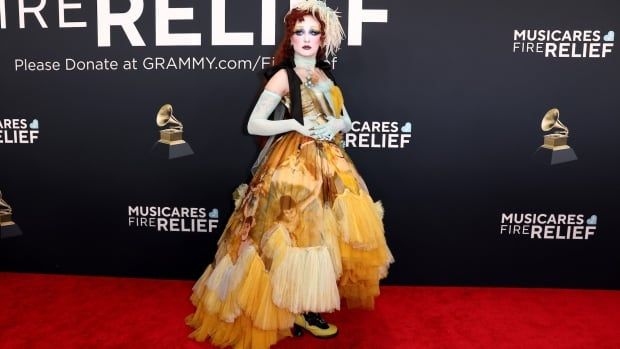 A woman on the red carpet wearing a voluminous yellow dress, feather accessory on her head and elbow-length gloves. 