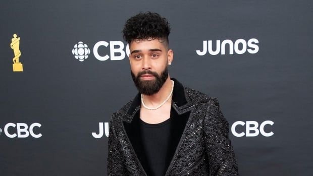 Man in shiny black suit posing on red carpet.