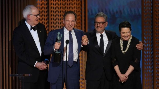 Four people (three men and one woman) accept an award behind a microphone