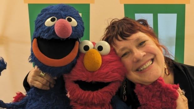 A woman grinning next to Elmo and Grover of Seasme Street fame.