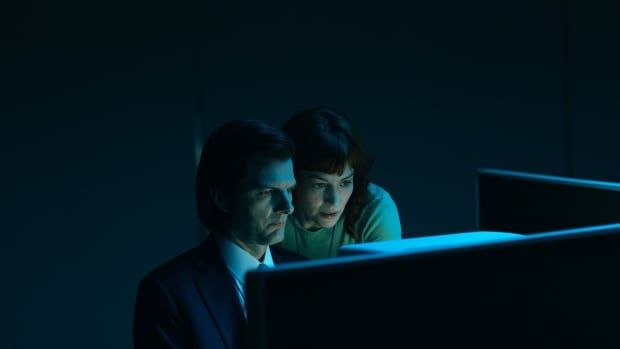 Two people lean over a computer in a dark room