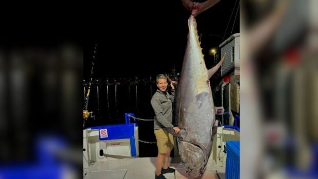 A woman smiles standing next to a big bluefin tuna on a boat 