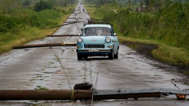 A car navigates a road littered with debris and fallen power lines.