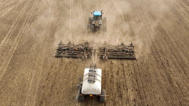 A tractor and seeding rig is seen from above as he drives along a bare field.