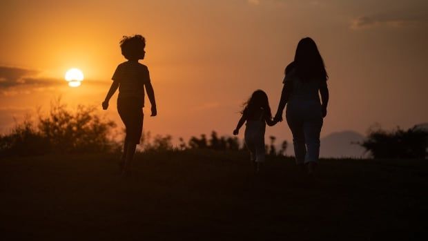 Silhouette of mother, daughter and son walking toward during sunset.