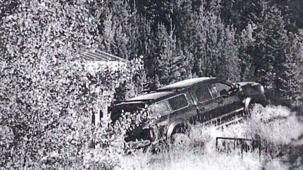 A truck with an elongated cab is parked in the wilderness, surrounded by trees.