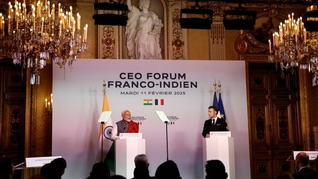 Two men speak from podiums in an ornate room with chandeliers hanging from the ceiling.