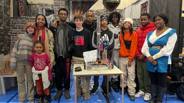 Ten students stand in their kiosk behind a desk with their robot.