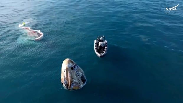 A boat is seen floating near a space capsule in the ocean.