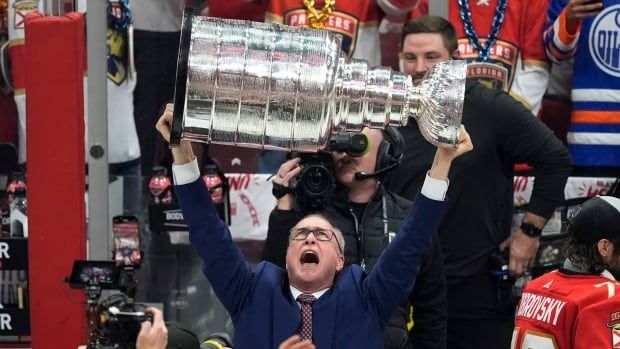 A men's hockey coach raises the Stanley Cup.