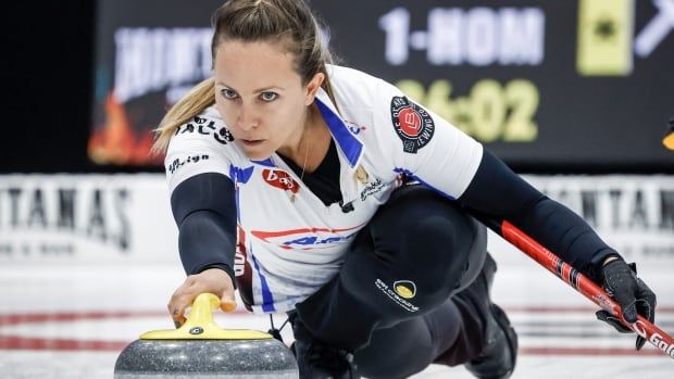 A female curling skip delivers a stone with her right hand.