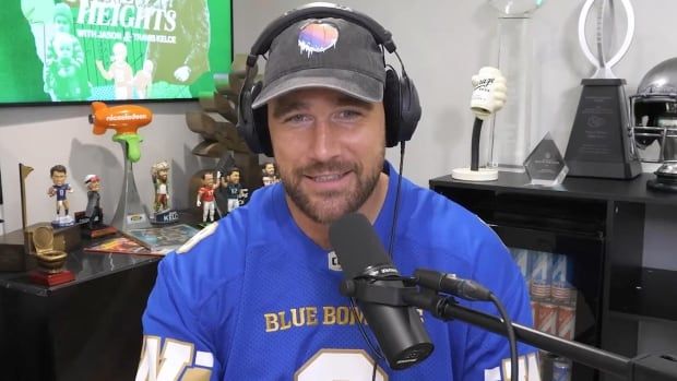 A man wearing headphones and a football jersey speaks into a microphone.