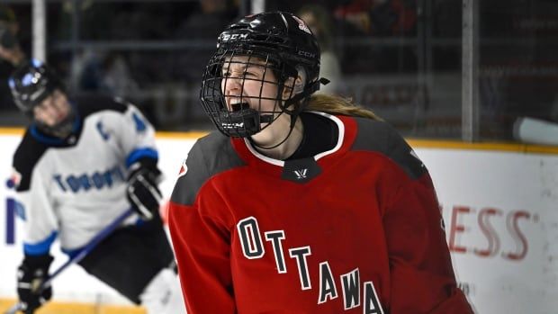 A women's hockey player screams out in celebration while an opponent looks dejected in the background.