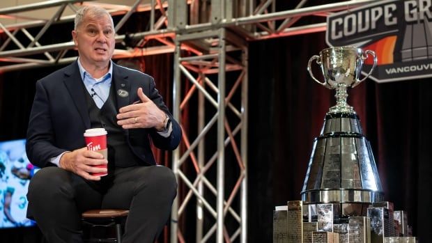 A man seated next to a trophy and holding a coffee cup, speaks during a news conference.