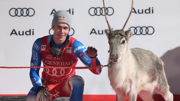 A men's skier poses for a photograph with a reindeer.