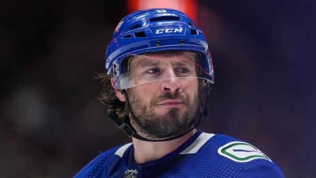 A white man wearing a blue hockey uniform scowls.